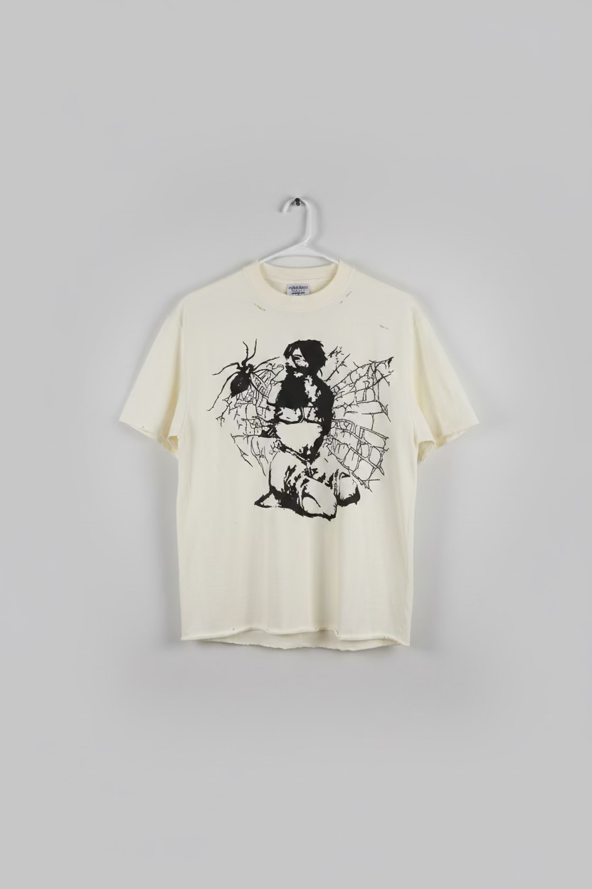 An off-white distressed t-shirt hanging on a hanger, featuring a black graphic print of a woman with a sword surrounded by a spider and web, next to a white t-shirt.